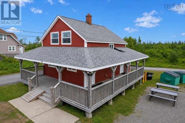Side view of the red commercial building, showcasing the porch, roof shingles, and a chimney against a blue sky. - 2011 Louisbourg Highway, Mira Road