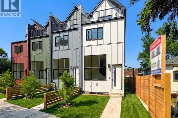 Modern townhouse exterior with white and grey metal siding, grass lawns and wood fences under a blue sky. - 2018 12 Avenue Sw, Calgary