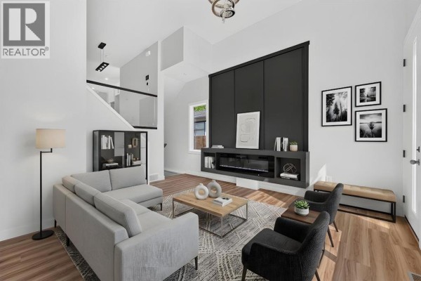Living room with a grey sectional sofa, dark accent chairs, and a modern fireplace on a dark grey feature wall. - 2018 12 Avenue Sw, Calgary