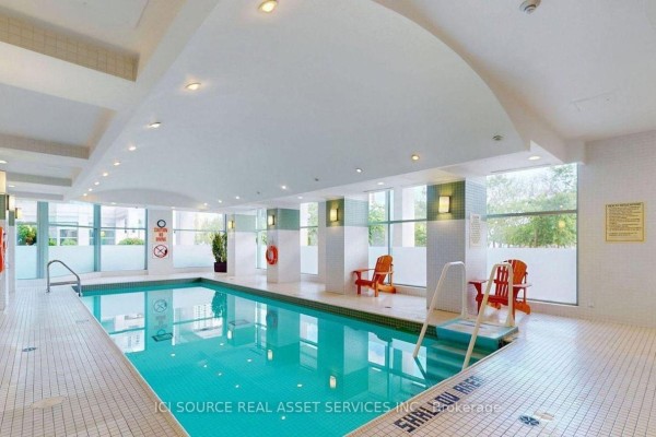 Indoor swimming pool with lounge chairs and windows overlooking outdoor greenery. - 2019 - 230 Queens Quay W, Toronto