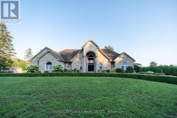 Front exterior view of a large stone house with a grand arched entryway and manicured lawn. - 20190 County Rd 2 Road, South Glengarry