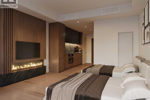 Bedroom with two beds, a fireplace, a television, and a small kitchenette area. - 202, 1724 Bow Valley Trail, Canmore