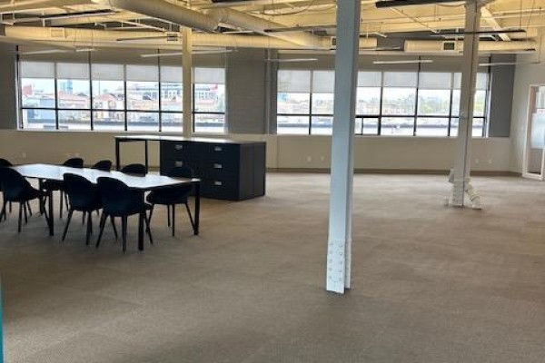 Large open office space with a meeting table, black chairs, and filing cabinet near windows. - 202 - 109 Vanderhoof Avenue, Toronto