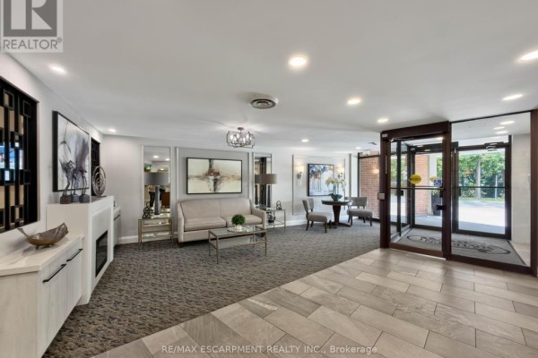 Apartment building lobby with seating area, mirrored walls, and grey tile floors. - 202 - 1230 Marlborough Court, Oakville