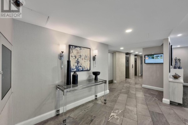 Building hallway with elevators, decorative table, artwork, and grey patterned wallpaper. - 202 - 1230 Marlborough Court, Oakville