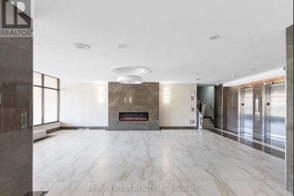 Building lobby with modern electric fireplace, marble floors, and elevator doors. - 202 - 130 Neptune Drive, Toronto