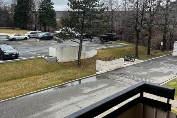 View from a balcony of a paved parking lot with cars and grassy areas. - 202 - 130 Neptune Drive, Toronto