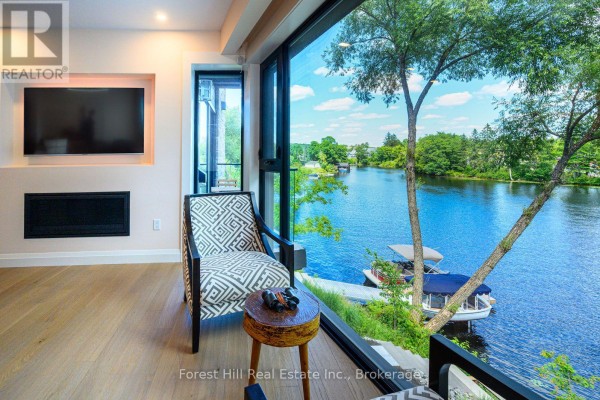 Interior view of a living space with a TV and fireplace, looking out to a lake. - 202 - 32 Brunel Road S, Huntsville