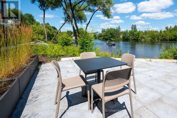 Outdoor patio with a table and four chairs, overlooking a calm lake with green trees. - 202 - 32 Brunel Road S, Huntsville