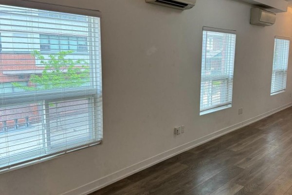 Interior room with white walls, wood-look flooring, blinds on windows, and air conditioning units. - 202 - 377 Church Street, Toronto
