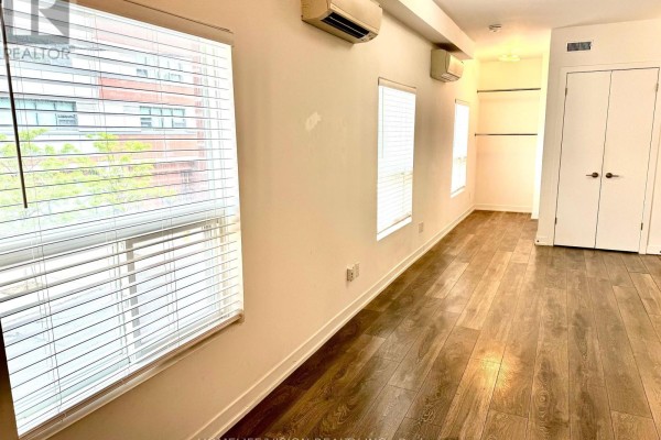Interior room with wood-look flooring, white walls, blinds on windows, air conditioning units, and double doors. - 202 - 377 Church Street, Toronto