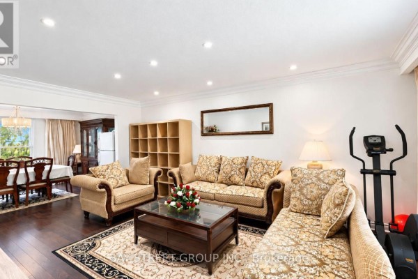Living room with a sofa, armchairs, coffee table, and exercise equipment. - 202 - 5 Elmira Court, Toronto