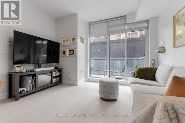 Bright living room with a white sectional sofa, ottoman, and large windows overlooking the balcony. - 202 - 68 Merton Street, Toronto