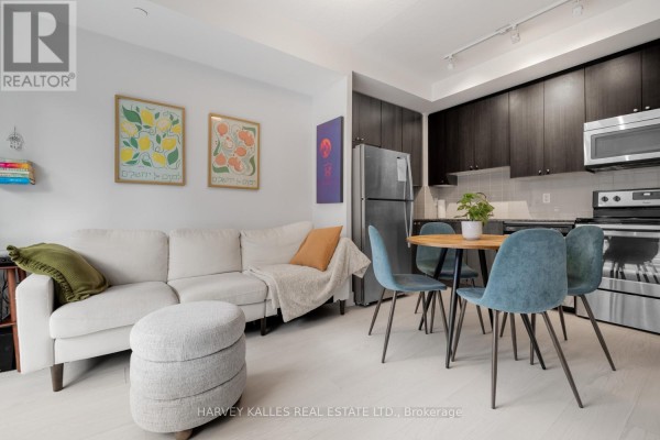 Compact dining area with a round table, blue chairs, and a stainless steel refrigerator in the kitchen. - 202 - 68 Merton Street, Toronto