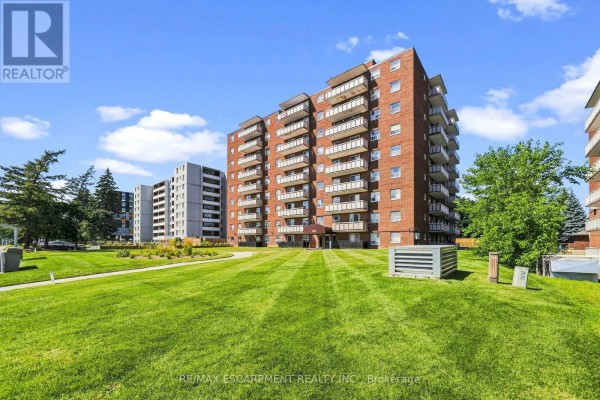 Side view of a brick apartment building with balconies and green lawn areas. - 202 - 851 Queenston Road, Hamilton