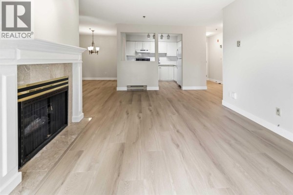 Living room with yellow walls, fireplace, and large windows overlooking greenery. - 202 1148 Westwood Street, Coquitlam