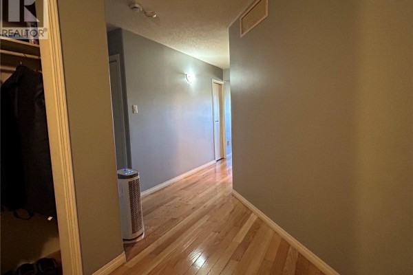 Interior hallway with beige walls, hardwood floors, and doors leading to other rooms. - 202 12 Cundall Drive, Estevan