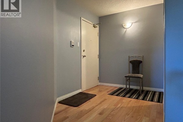 Apartment entryway with beige walls, white door, metal chair, and striped rug on hardwood floor. - 202 12 Cundall Drive, Estevan