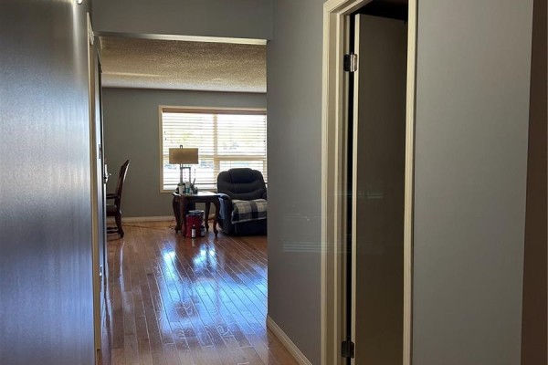 View down hallway into a living area with a window, armchair, and dining chair. - 202 12 Cundall Drive, Estevan