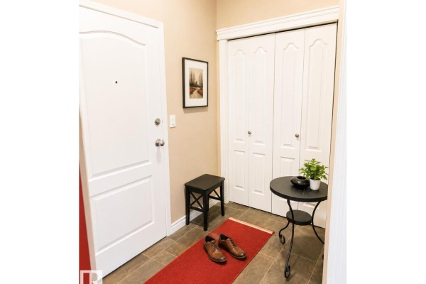 Apartment entryway with a red rug, black stool, small table, and white double doors. - #202 16715 100 Av Nw, Edmonton
