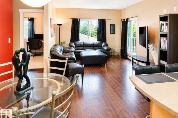Living room with dark wood floors, black leather sectional sofa, and glass dining table. - #202 16715 100 Av Nw, Edmonton