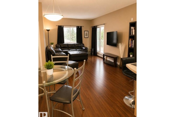 Living room with black leather sofa, television, bookshelf, and dining area with glass table. - #202 16715 100 Av Nw, Edmonton