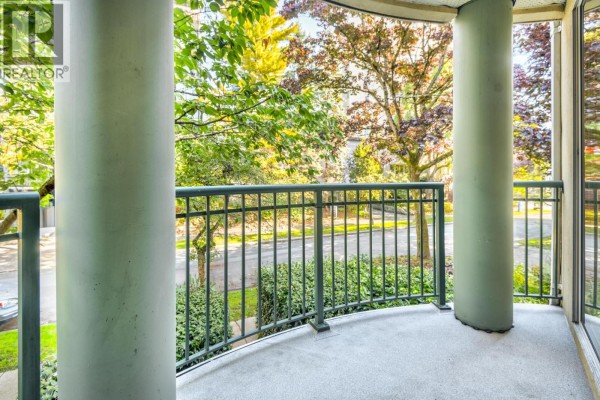 Curved balcony with concrete floor, metal railing, and views of trees and street. - 202 1928 Nelson Street, Vancouver