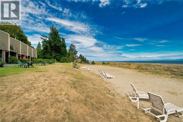 Exterior of a three-story apartment building with a car parked in front. - 202 3295 Island Hwy W, Qualicum Beach