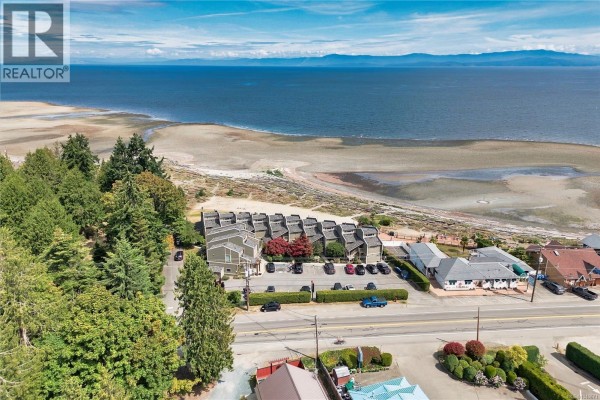 Compact kitchen with white cabinets, wood-paneled ceiling, and a staircase. - 202 3295 Island Hwy W, Qualicum Beach