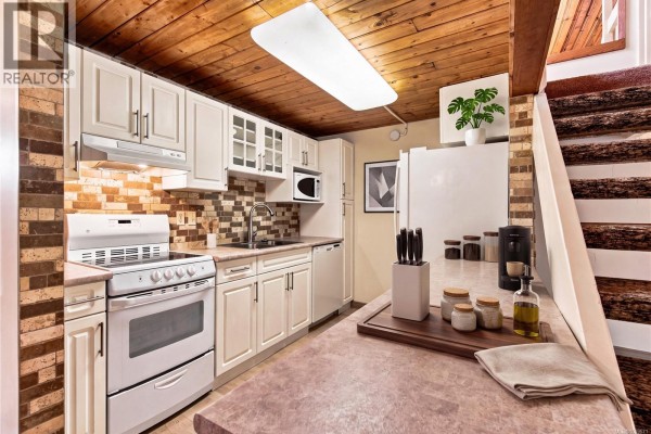 View of a galley kitchen with white cabinets and a wooden ceiling. - 202 3295 Island Hwy W, Qualicum Beach