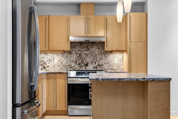 Open-concept kitchen with wood cabinetry, granite island, and stainless steel appliances. - 202 6591 Lincroft Rd, Sooke