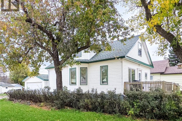 Side view of white siding house with green trim, wooden deck, and mature trees. - 202 6th Avenue E, Melville