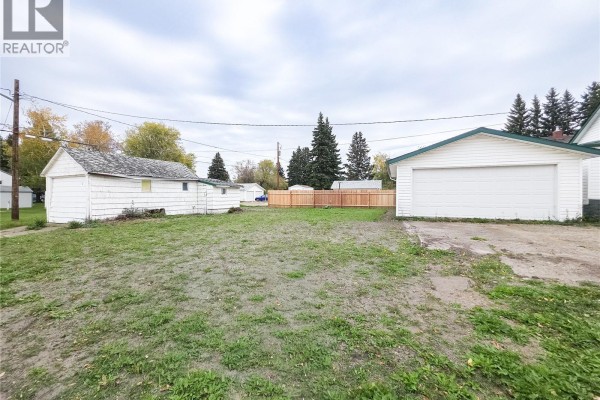 Backyard view of white siding house with detached garage, storage shed, and wooden fence. - 202 6th Avenue E, Melville