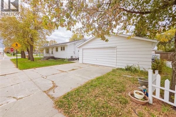 View of the white bungalow and attached garage from the driveway, with a sidewalk and street. - 202 7th Avenue W, Melville