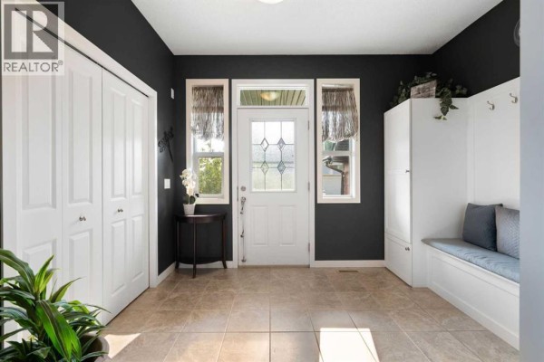 Foyer with a white front door, tiled floor, and a built-in white storage bench. - 202 Boulder Creek Court Se, Langdon