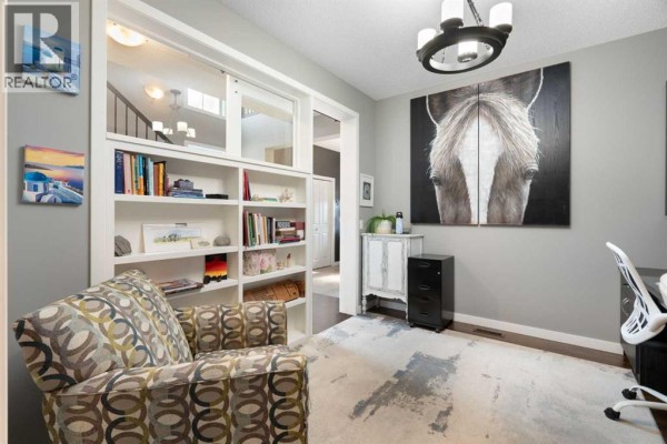 Home office with grey walls, a patterned armchair, built-in bookshelves, and a large horse painting. - 202 Boulder Creek Court Se, Langdon