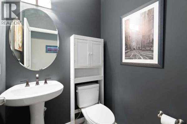Powder room with dark grey walls, a pedestal sink, a toilet, and a circular mirror. - 202 Boulder Creek Court Se, Langdon