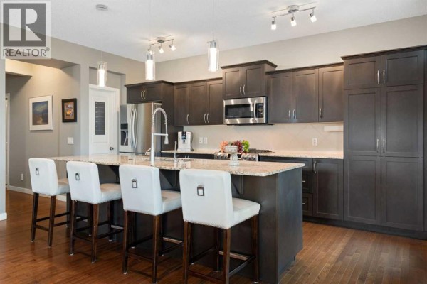 Kitchen with dark grey cabinets, a granite-topped island with white bar stools, and stainless steel appliances. - 202 Boulder Creek Court Se, Langdon