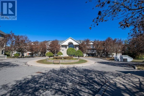 Exterior view of the apartment building with trees and a circular driveway. - 202 C - 1099 Clonsilla Avenue, Peterborough