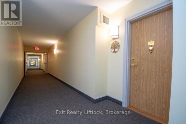Interior hallway with beige walls, grey carpet, and light fixtures. - 202 C - 1099 Clonsilla Avenue, Peterborough