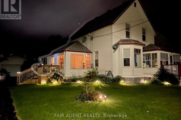 Exterior of a white house at night with deck lights and landscape illumination. - 202 Water Street, Thessalon