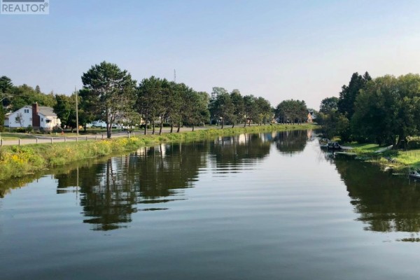 Wide view of a calm canal with reflections of trees and houses under a clear sky. - 202 Water Street, Thessalon