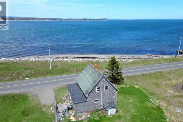 Rear aerial view of a two-story house with gray shingles and a green roof, adjacent to the ocean. - 202 White Head Road, White Head Island