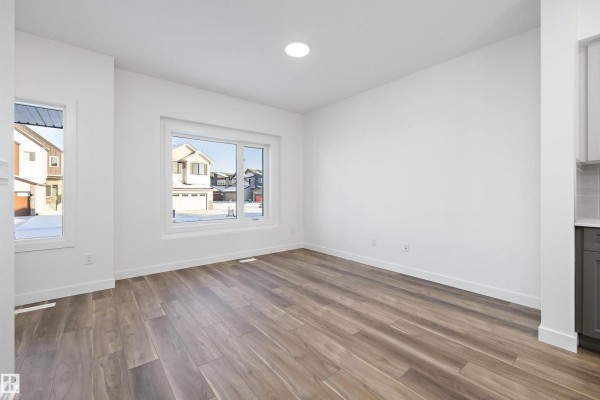 Living room with white walls, wood-look flooring, and large windows overlooking the street. - 2020 191 St Nw, Edmonton