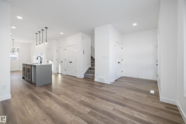 Open-concept living area with grey island, dark wood cabinets, and carpeted stairs. - 2020 191 St Nw, Edmonton