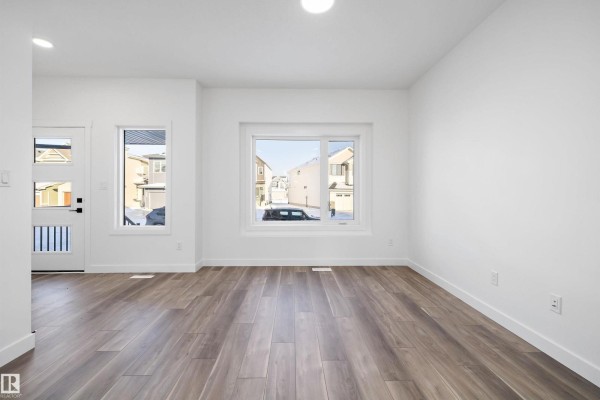 Interior view showing white walls, wood-look flooring, and a large window with a view of houses. - 2020 191 St Nw, Edmonton