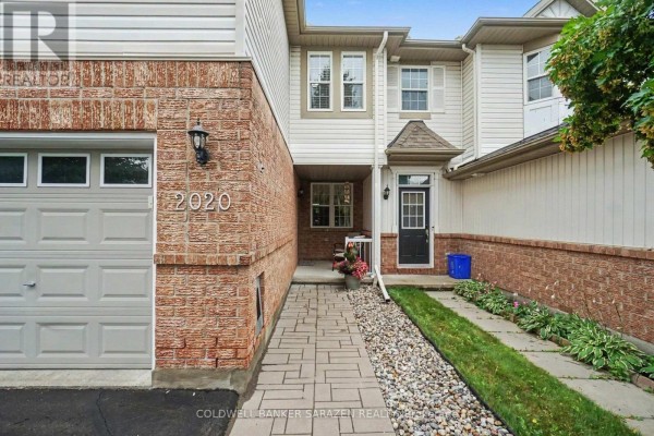 Front entrance of the townhouse with a paved walkway, stone garden bed, and number 2020. - 2020 Breezewood Street, Ottawa