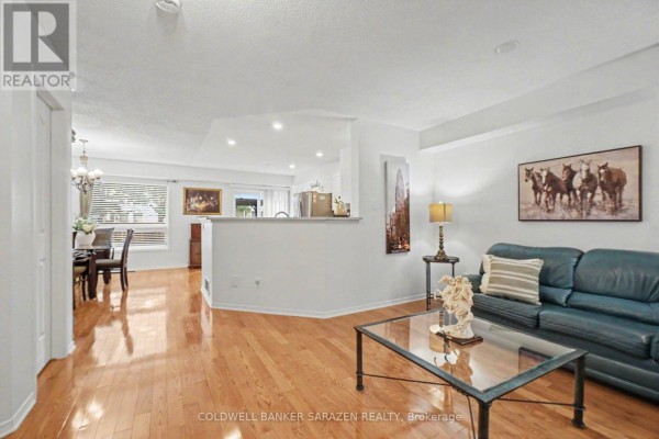Living room with hardwood floors, a leather sofa, glass coffee table, and view of dining area. - 2020 Breezewood Street, Ottawa