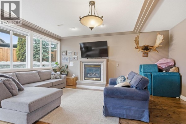 Living room with a gas fireplace, large windows, and hardwood floors. - 2025 Panorama Court, Kamloops