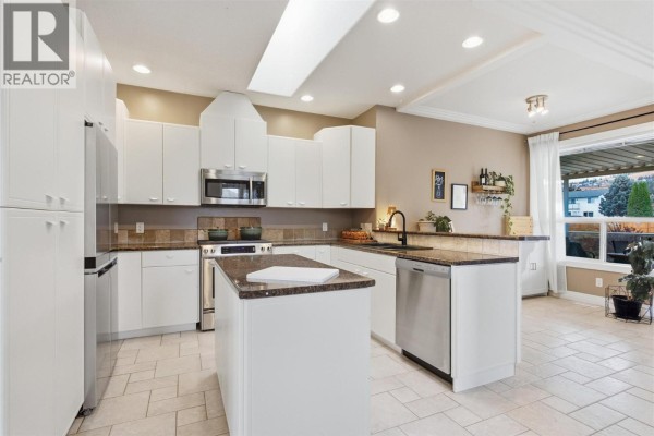 White kitchen with granite countertops, stainless steel appliances, and an island. - 2025 Panorama Court, Kamloops